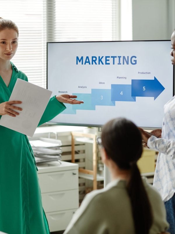 Young businesswoman with report pointing at screen with graphs and giving new information to her colleagues at training